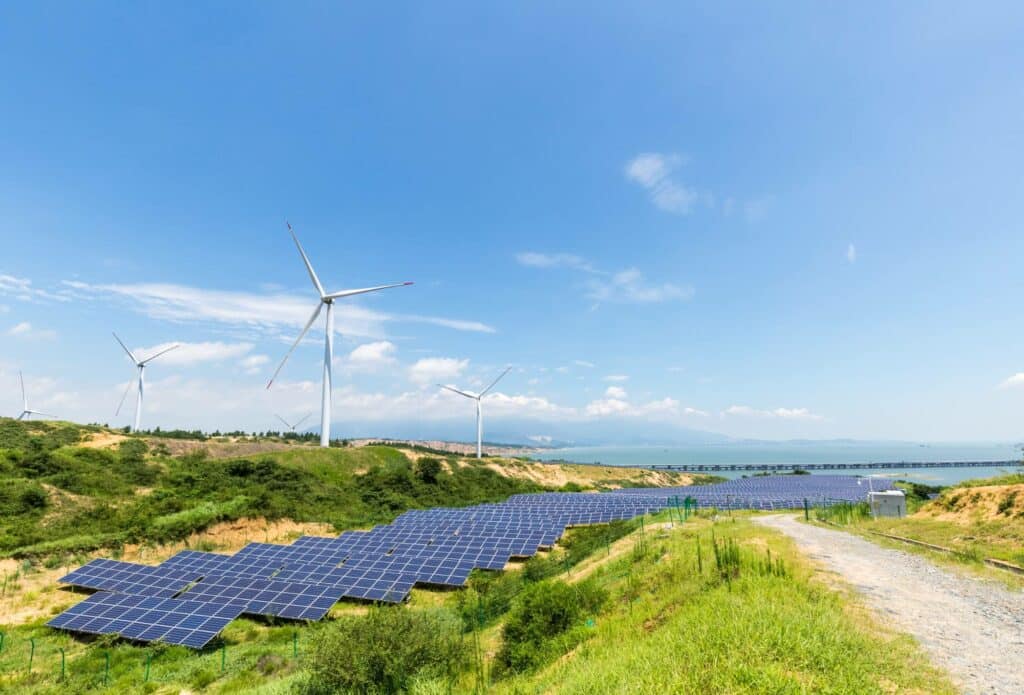 Windmills, solar panels, and lush green foliage line a country highway.